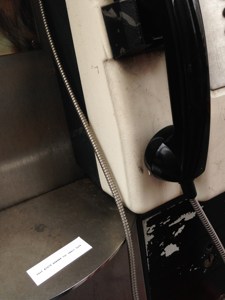 Small business card placed next to a public phone. The text on the card says "for small talk text xxx"